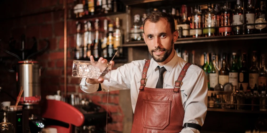 Professional bartender holding a cocktail shaker in breathable linen bartender shirts inside a modern bar environment