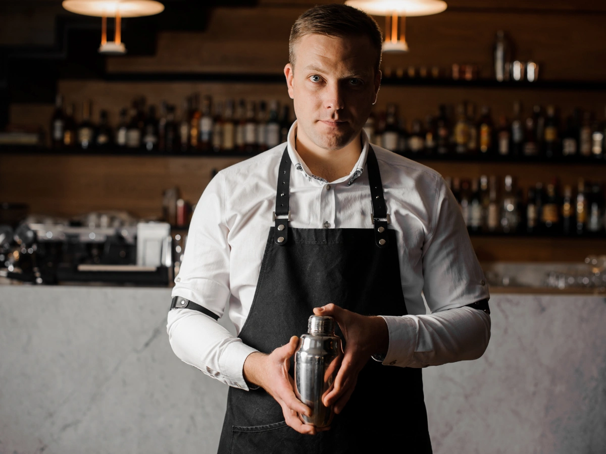 Head bartender standing confidently at a restaurant bar wearing breathable linen bartender shirts and a classic apron