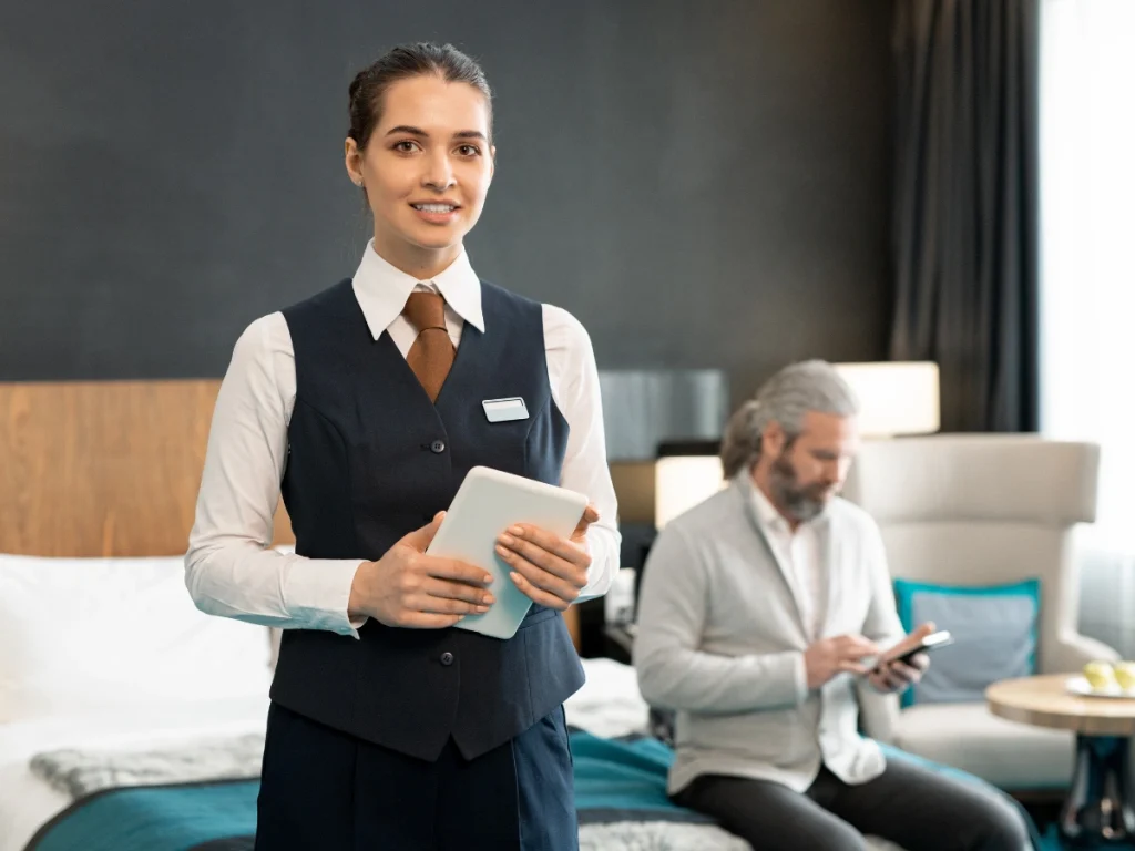 Hotel staff member in elegant hospitality uniforms assisting guest with tablet in luxury room