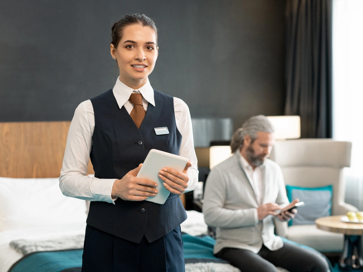 Hotel staff member in elegant hospitality uniforms assisting guest with tablet in luxury room